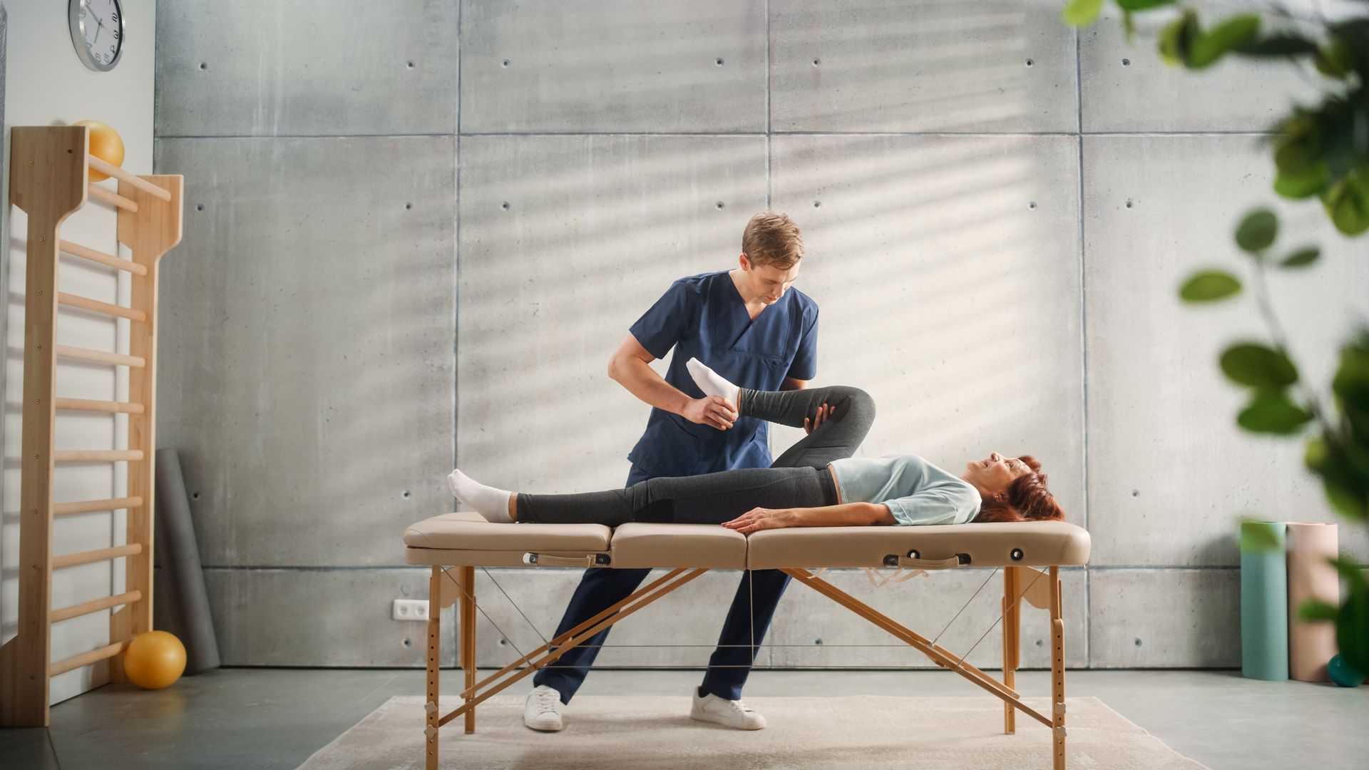 Physiotherapist stretching a patient on a treatment table in a bright clinic room