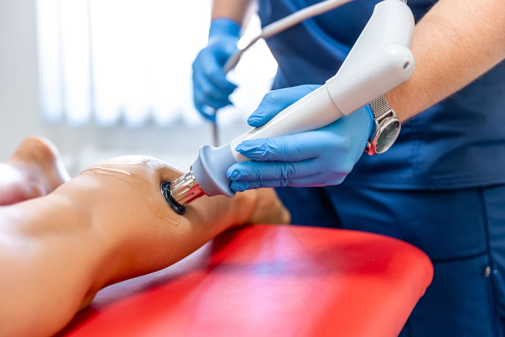 Person using a handheld treatment device on another person’s leg in a clinical setting