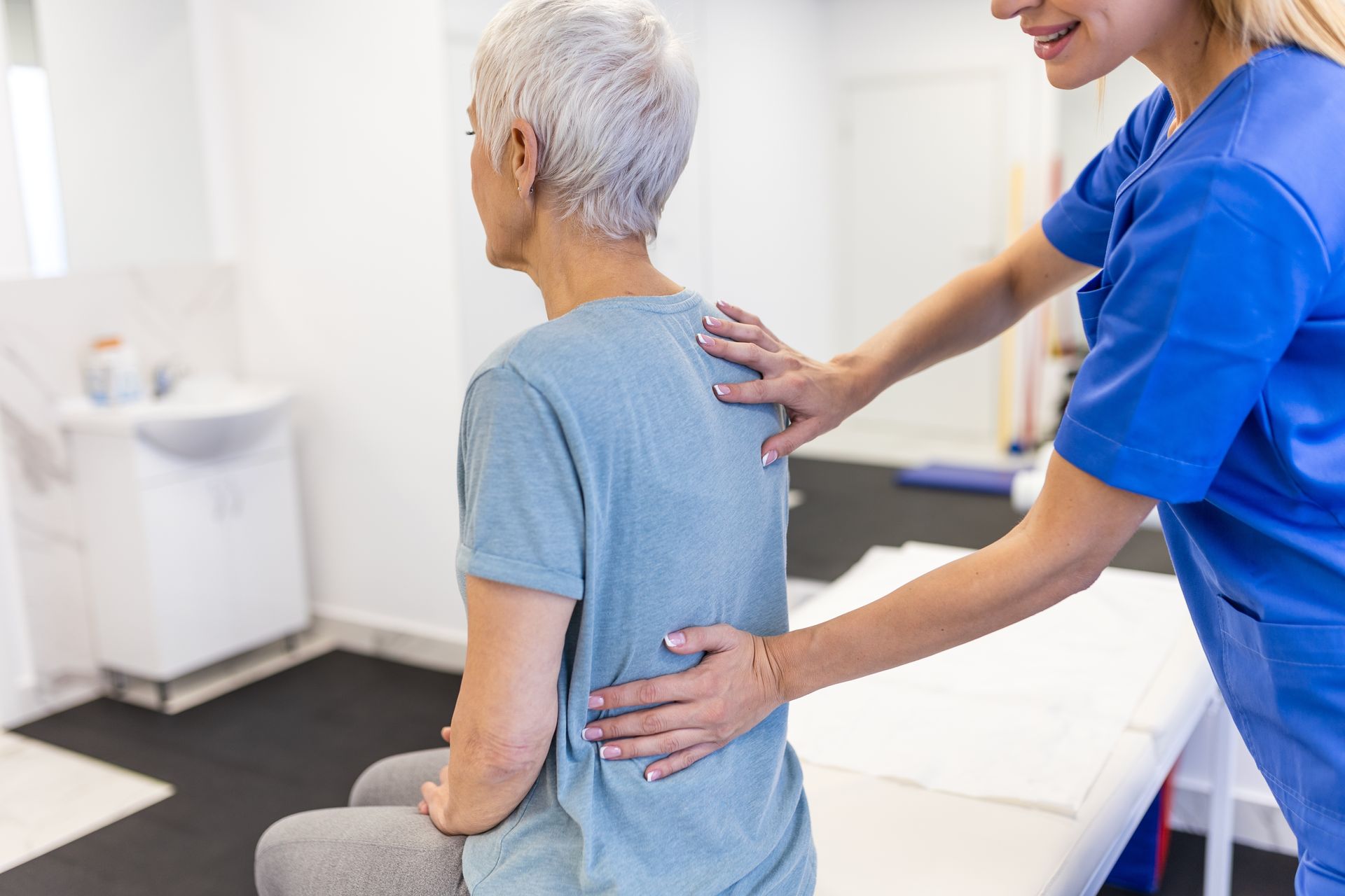 Caregiver helping a seated patient with back support in a bright clinic exam room