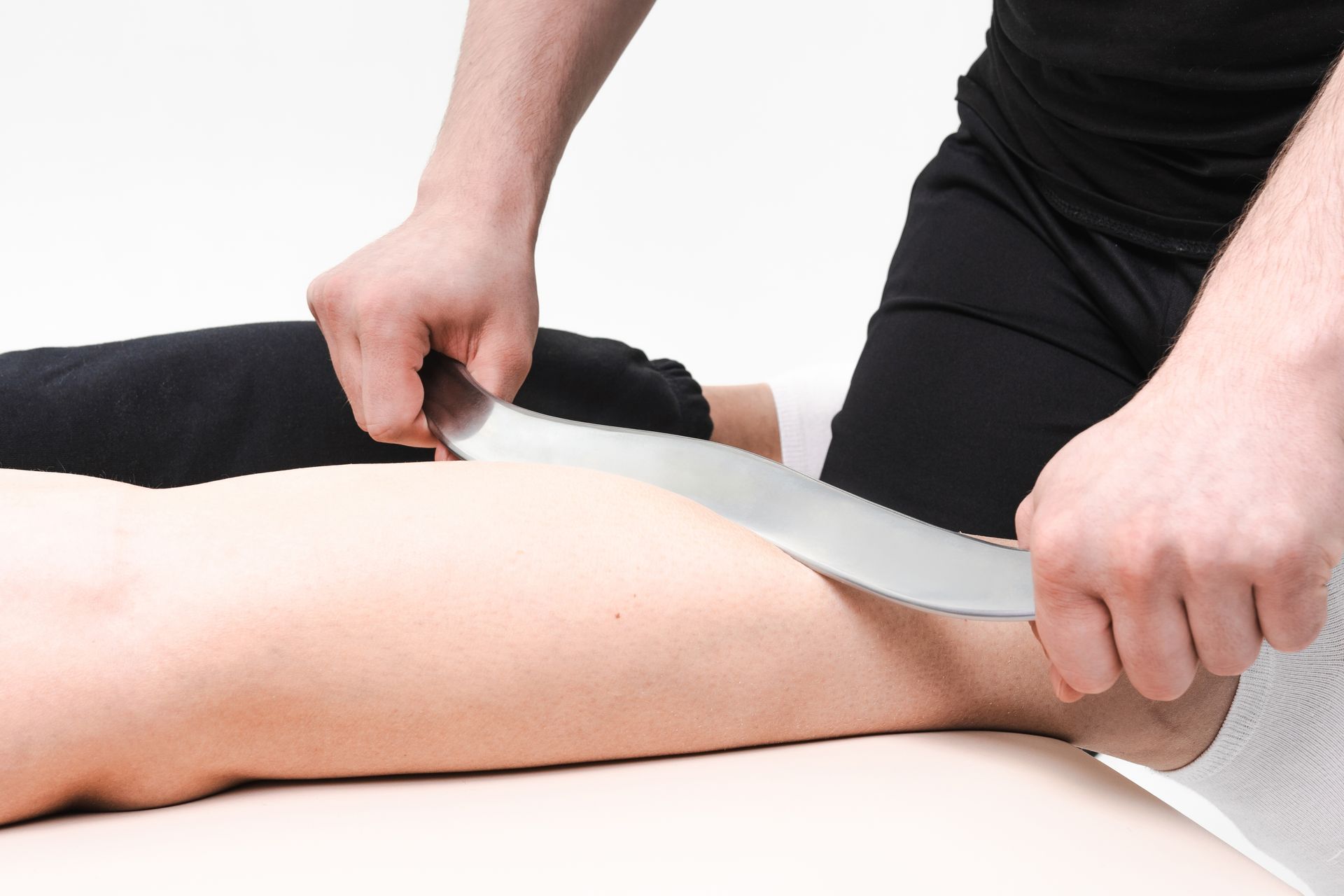 Hands using a massage tool on a person’s leg on a treatment table