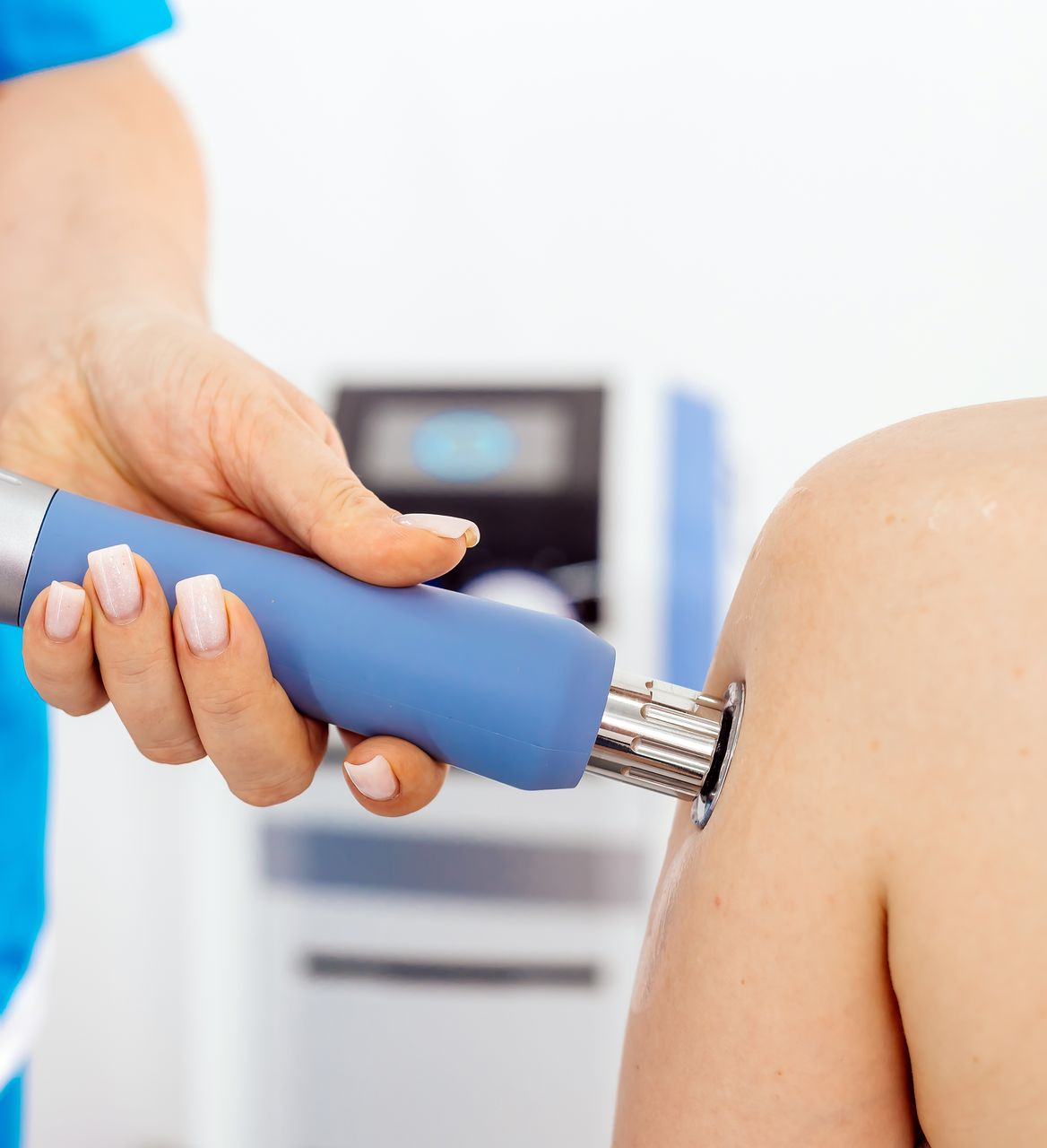 Hand holding a blue massage device against a person’s shoulder in a clinic setting