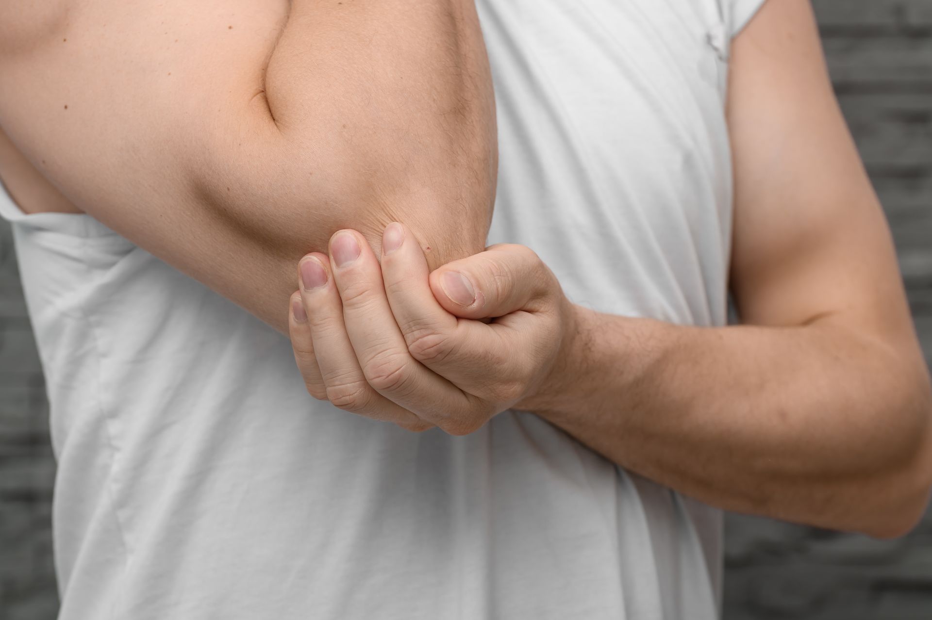 Person holding an elbow with the other hand, showing arm pain on a gray background