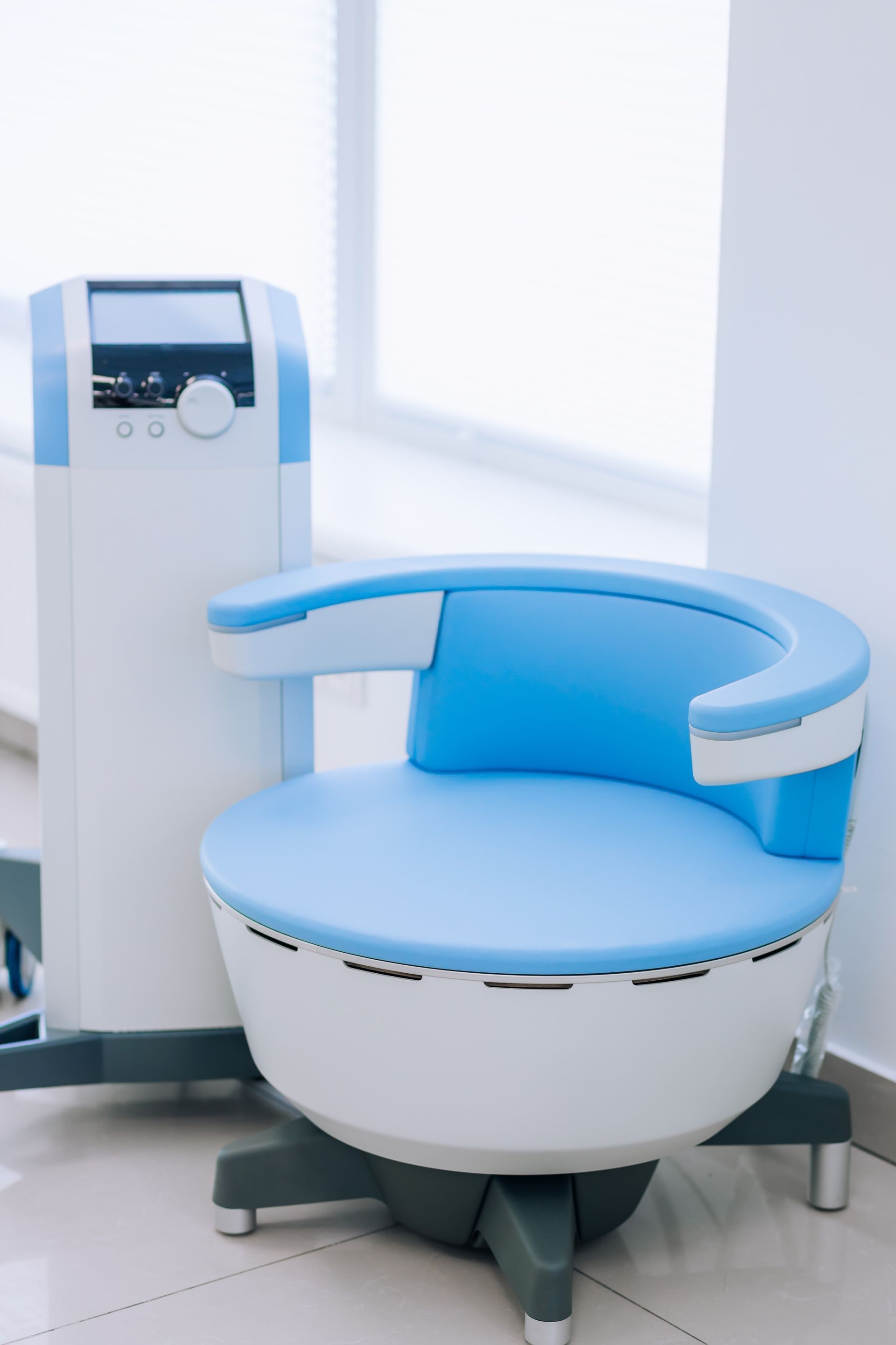 Blue and white medical chair with control console in a bright room