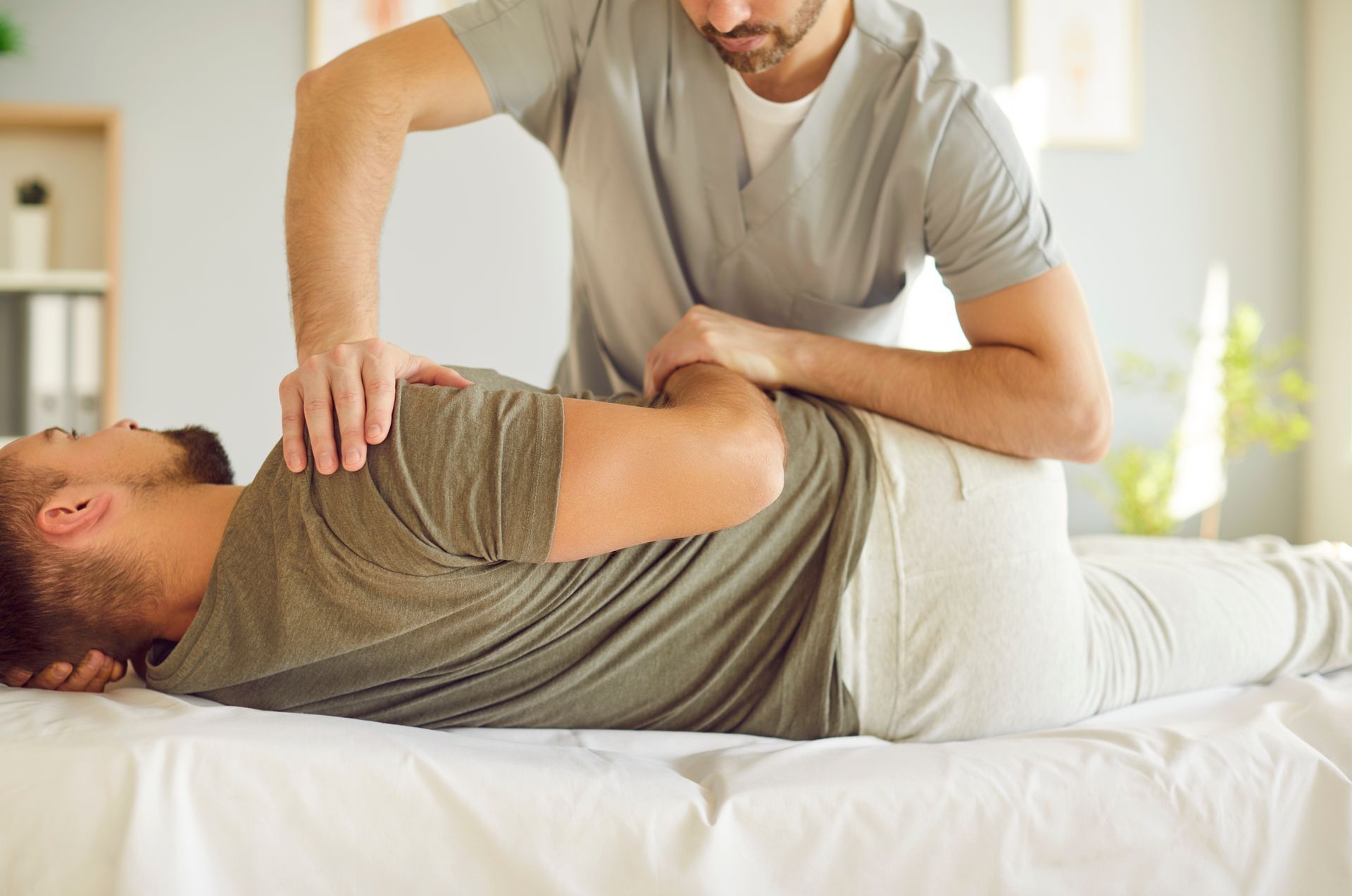 Physical therapist stretching a patient’s back on a treatment table in a bright room
