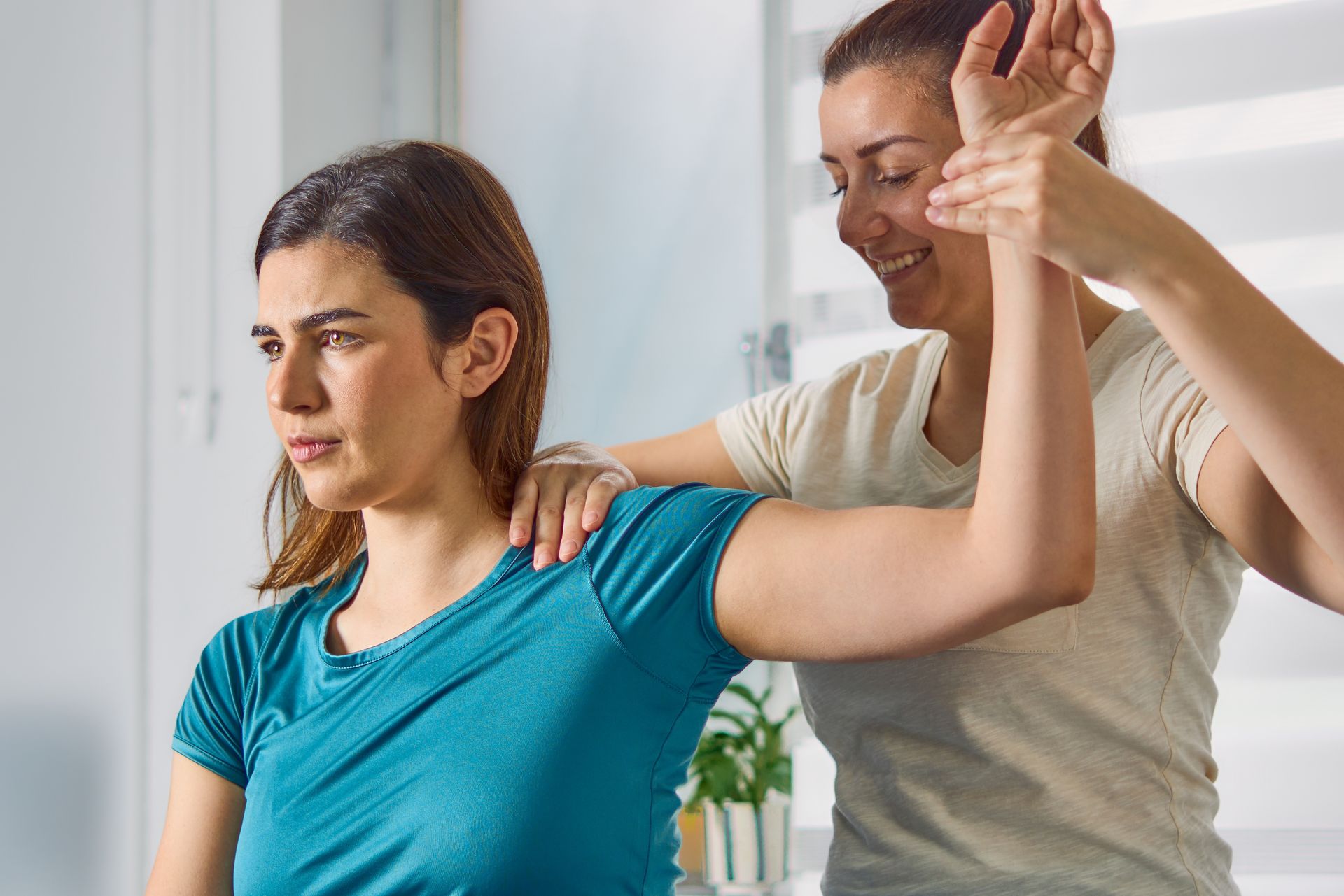 Woman receives shoulder stretch from therapist in bright room