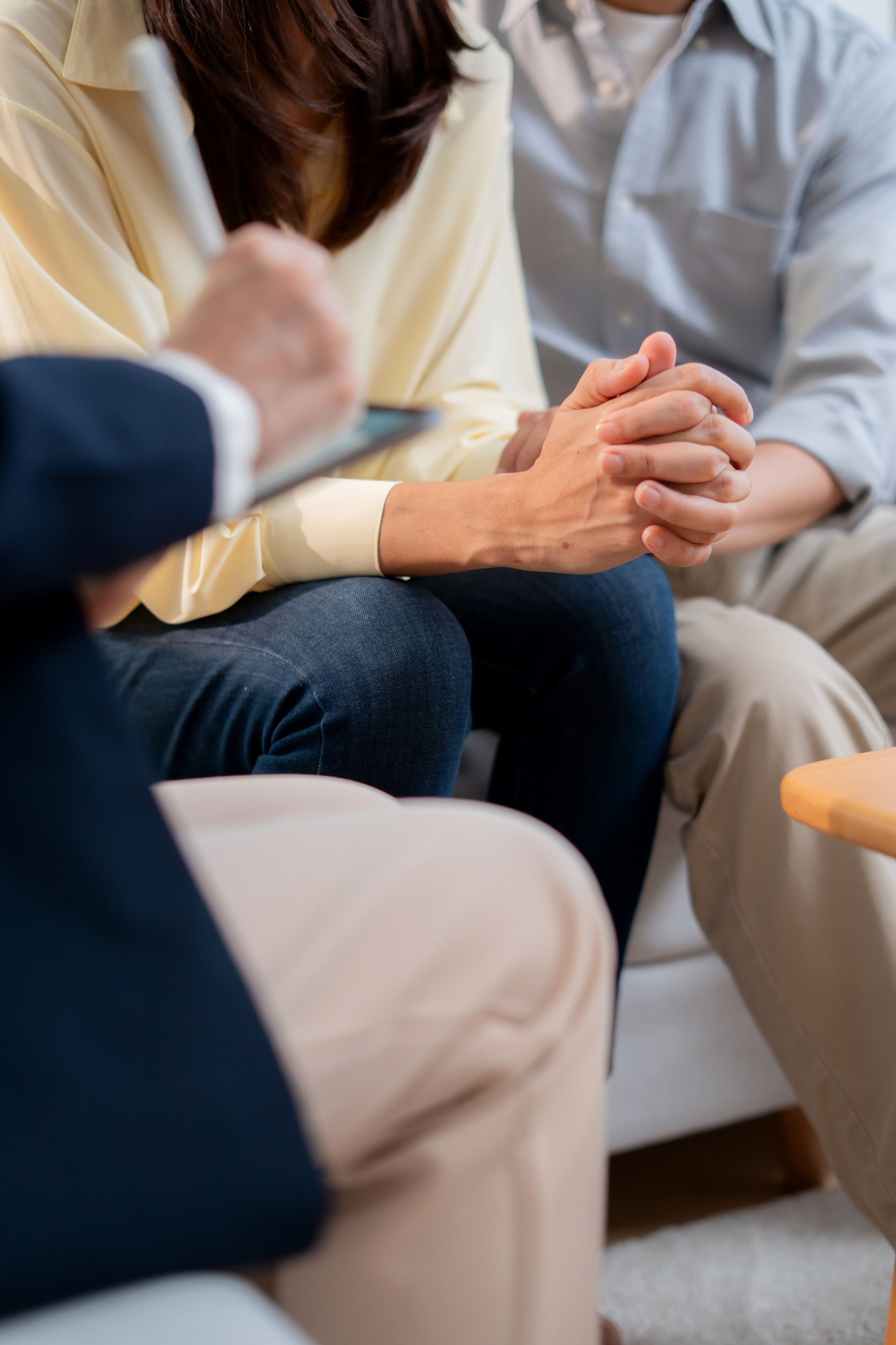 People seated in a counseling session, hands clasped in a supportive group discussion.