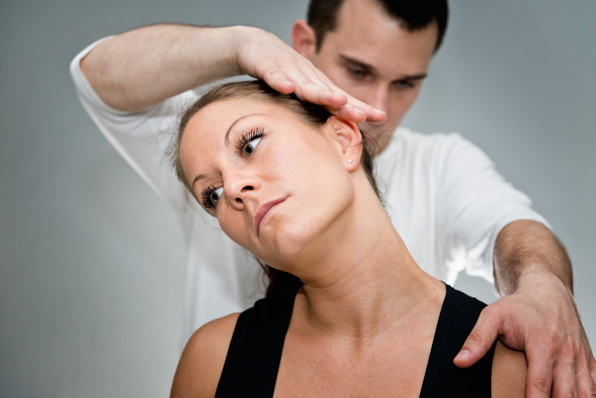 Therapist gently stretching a woman’s neck and shoulder in a clinical setting