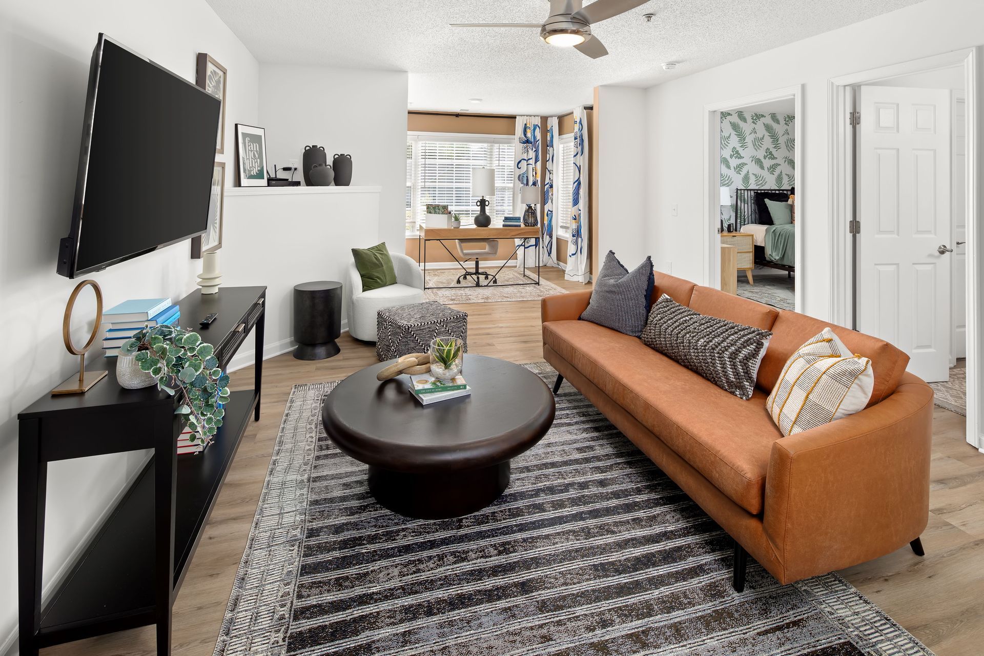 Living room with brown leather sofa, coffee table, rug, TV, and open to a home office.