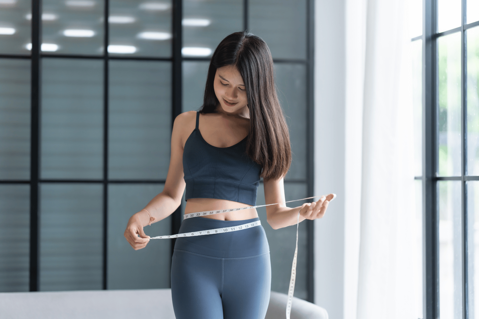 Woman in athletic wear measuring waist with a measuring tape.
