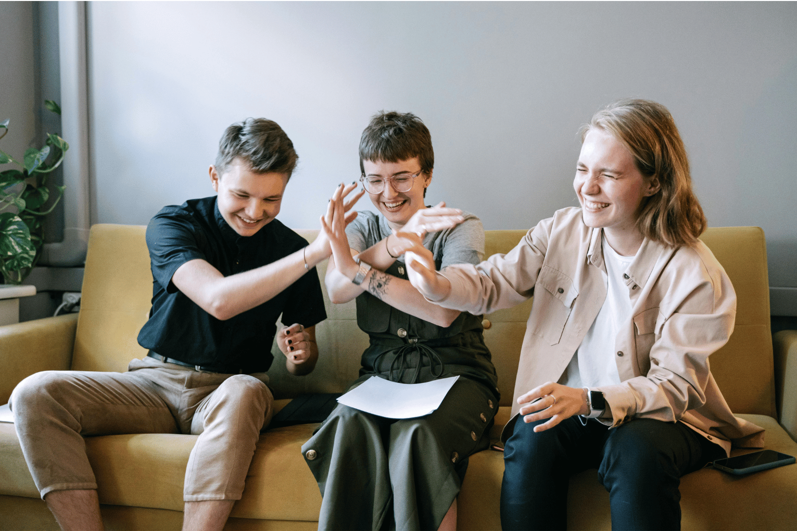 Three people seated on a yellow sofa, smiling and high-fiving.
