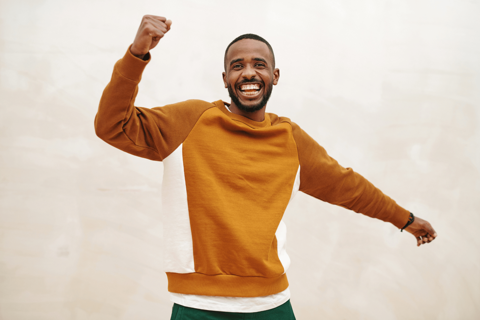 Man with a big smile and raised fist celebrates wearing an orange and white sweatshirt.