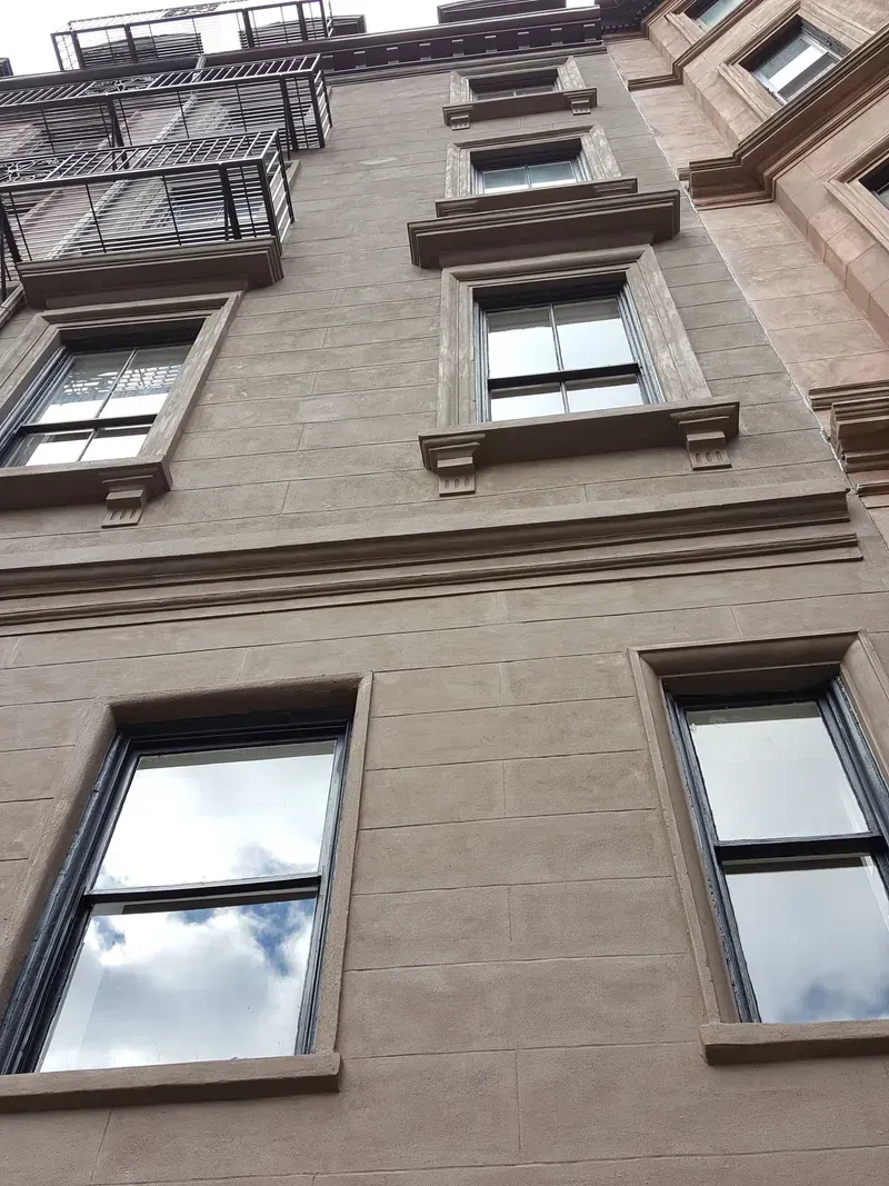 Brown brick building exterior with multiple windows, a fire escape, and decorative molding.