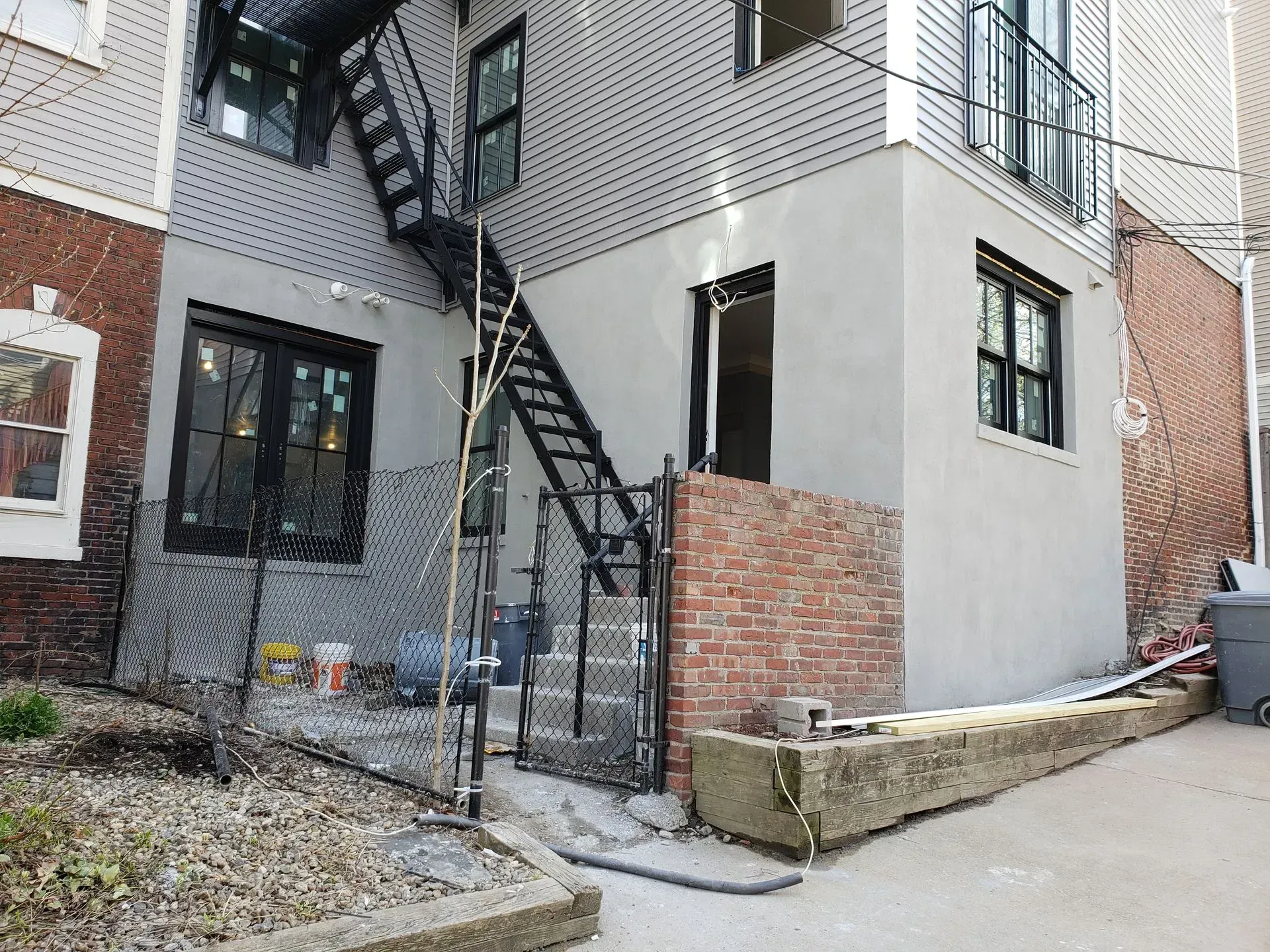 Exterior view of a building with a black fire escape, brick wall, and gray siding.
