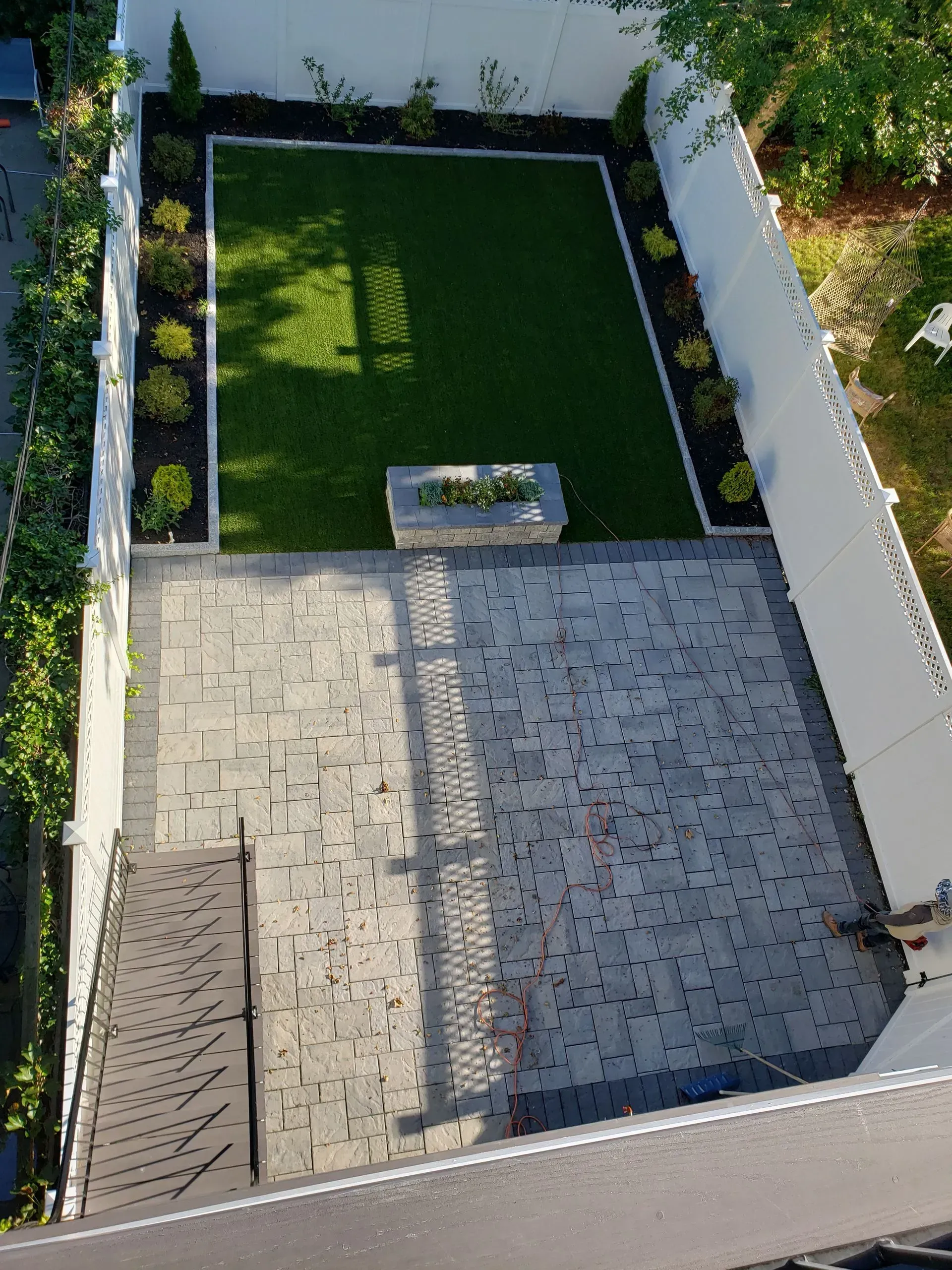 Patio with grey pavers, small lawn, flower bed, white fence.