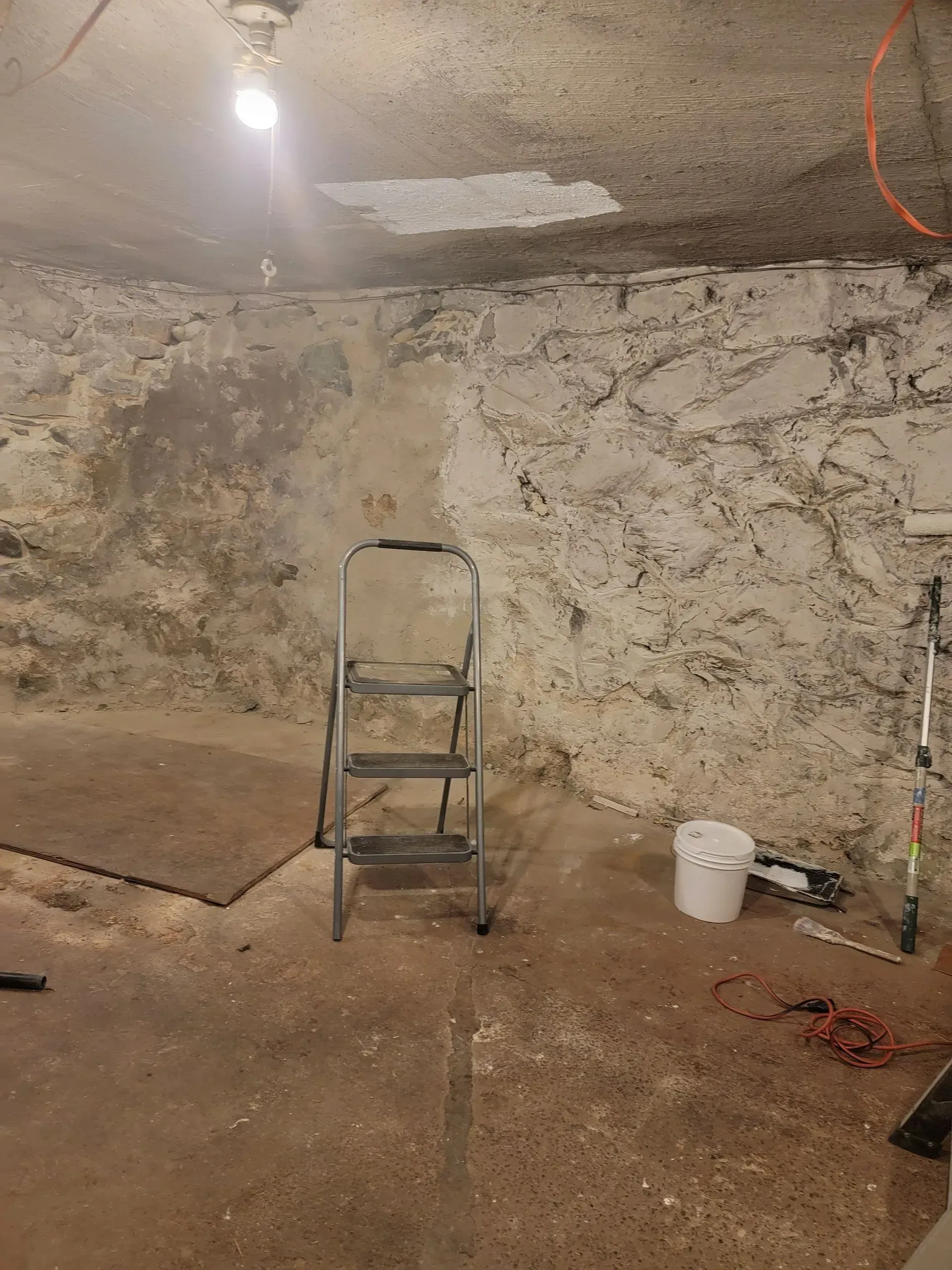 Basement interior with stone walls, a ladder, a bucket, and debris on the floor.