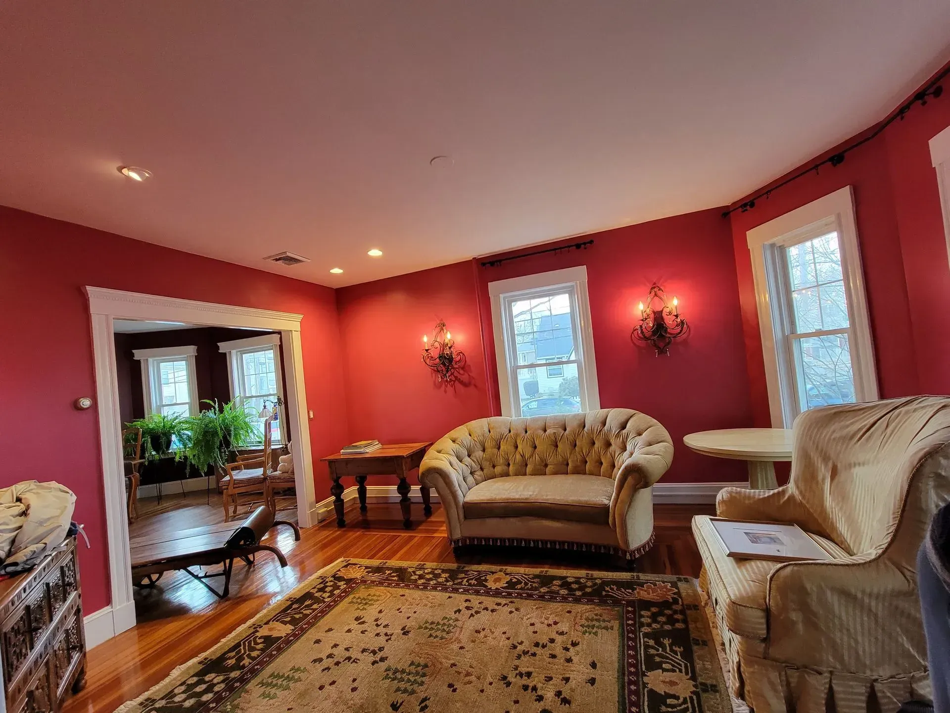 Living room with red walls, patterned rug, tufted sofa, and two windows.