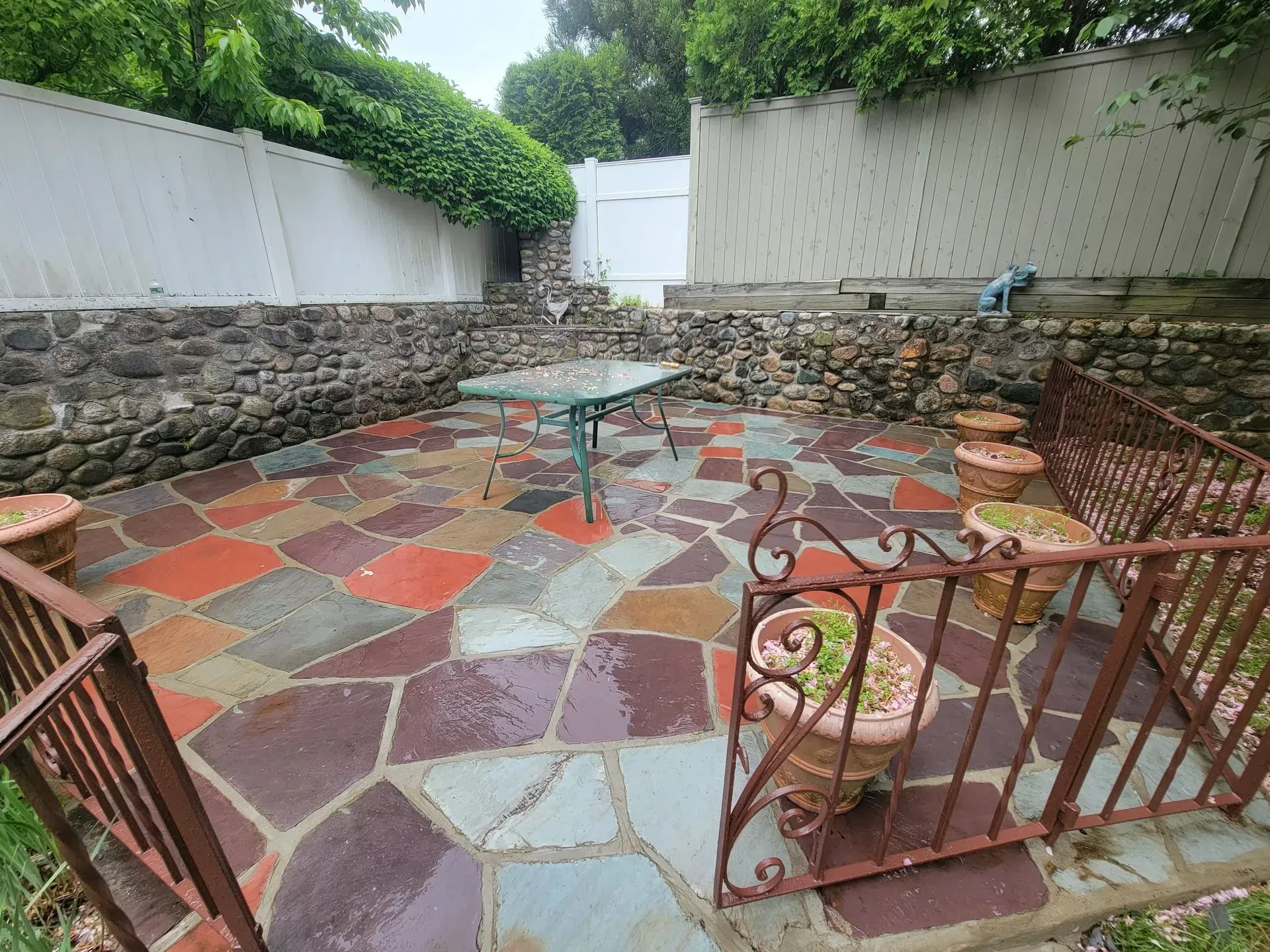 Patio with colorful flagstone, table, wrought iron railing, and stone and white walls.