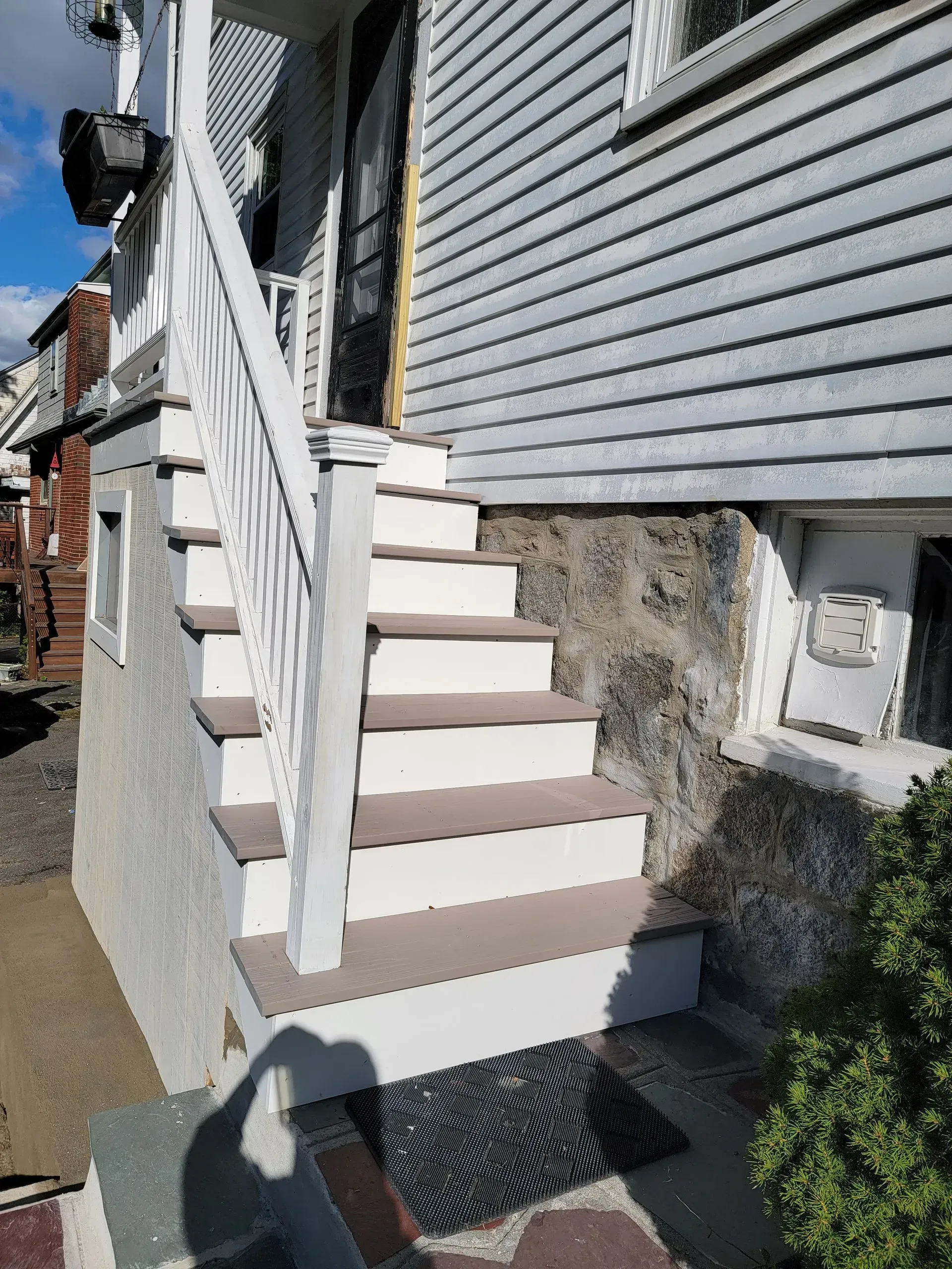 Exterior stairs leading up to a house. White railing, tan steps, and a doormat.
