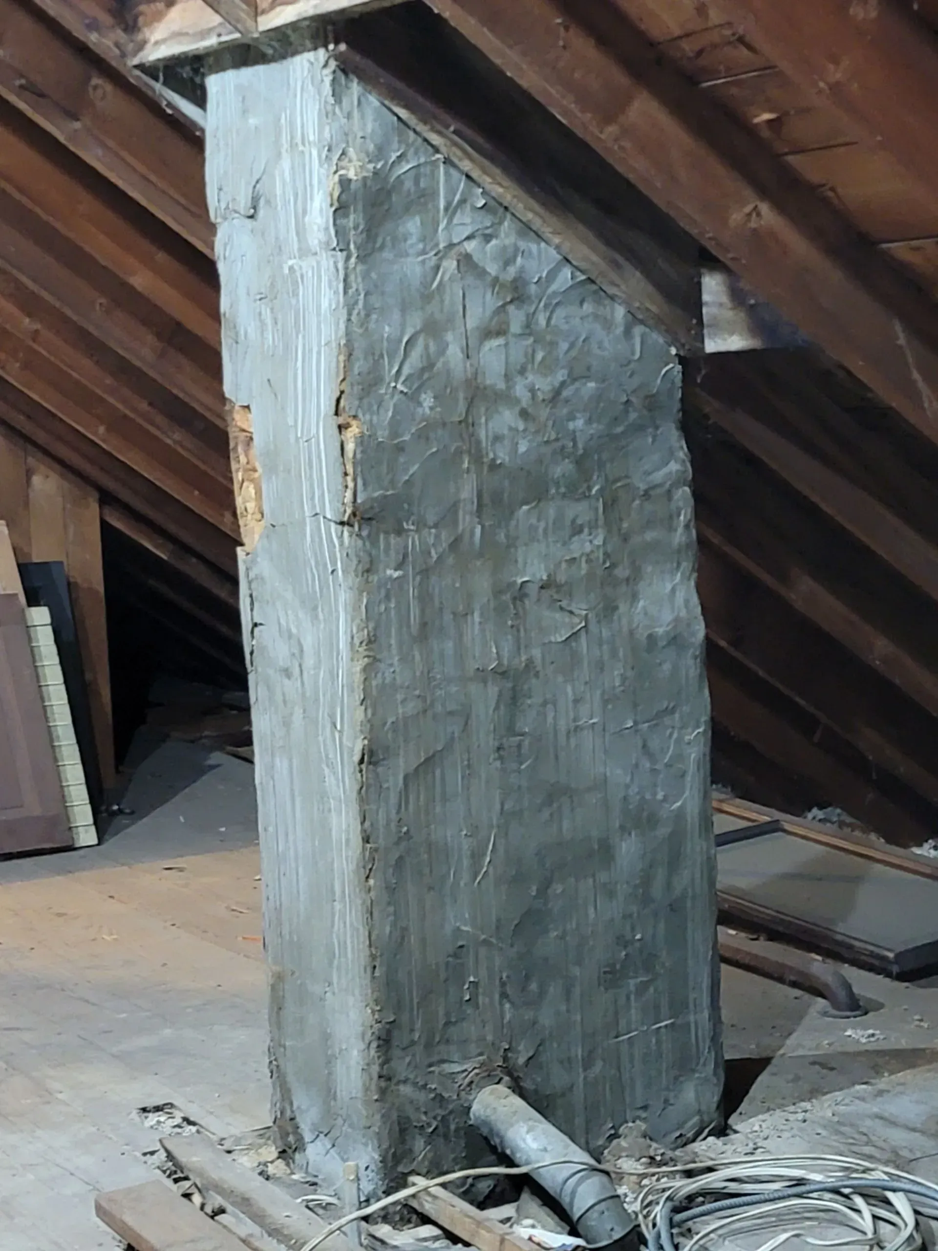 A gray, rectangular chimney in an attic with wooden beams and a slanted roof.