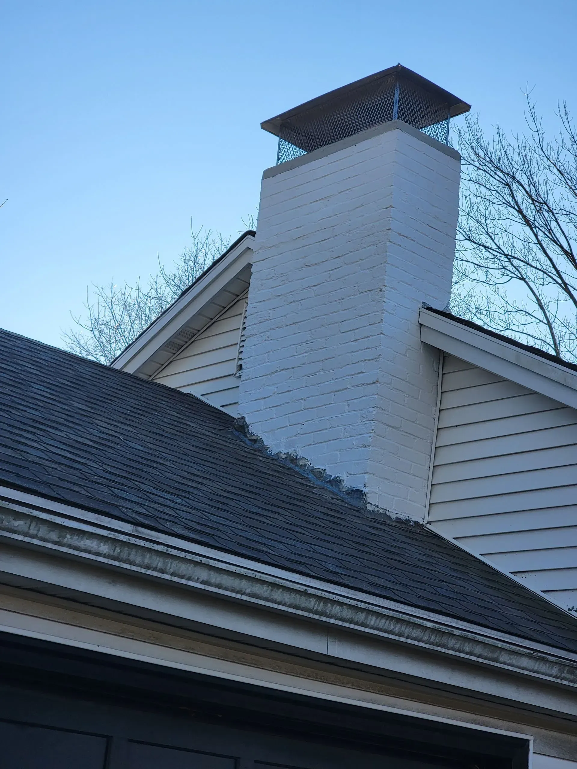 White brick chimney with a mesh top on a house with dark gray shingles.