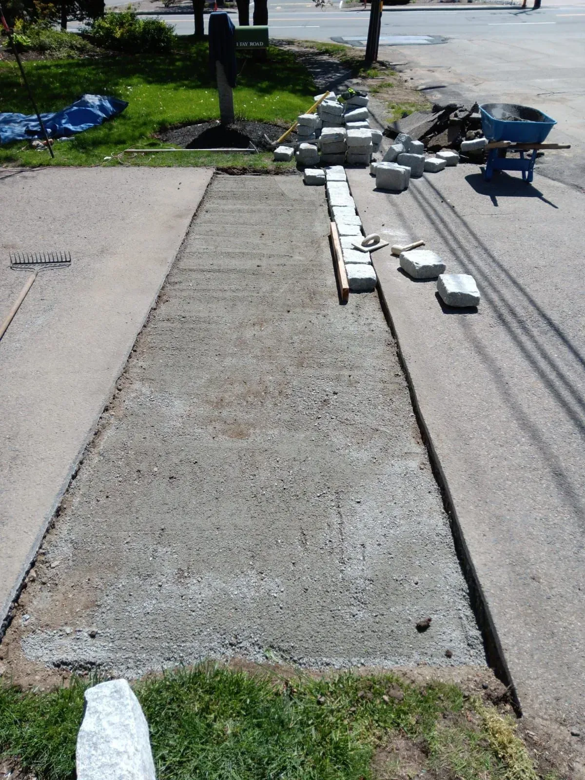 Concrete sidewalk section being renovated, with pavers and tools nearby.