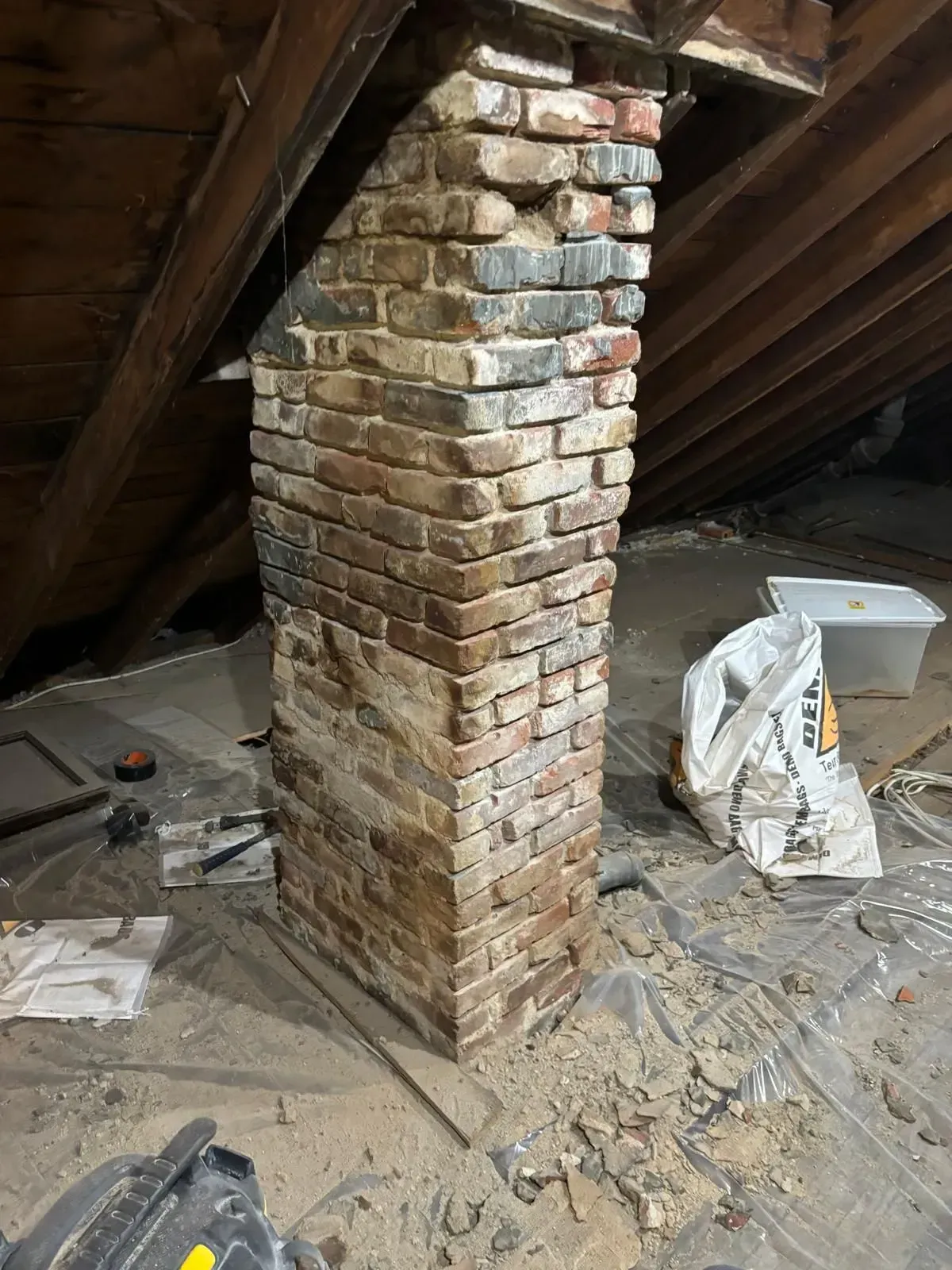Brick chimney in an attic, with wood beams, tarps, and debris.