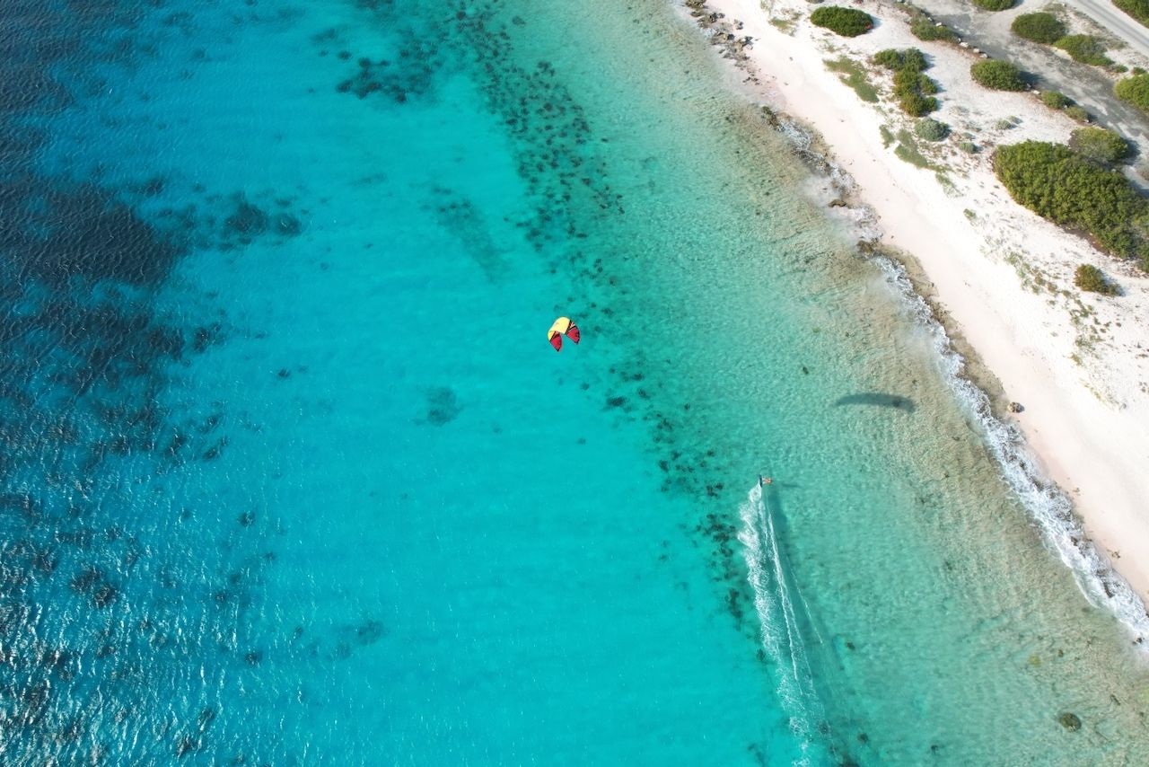 An aerial view of a person flying a kite in the ocean in the caribbean