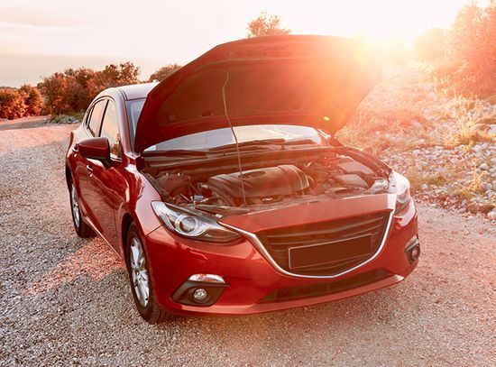 Red car with open hood on a gravel roadside at sunset