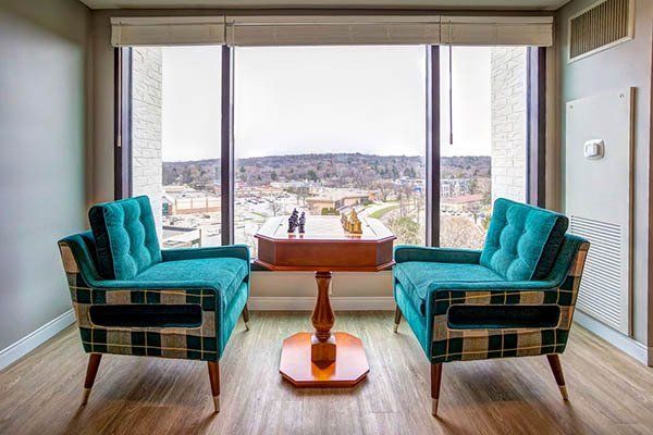 Two teal armchairs and small table face window with city view.