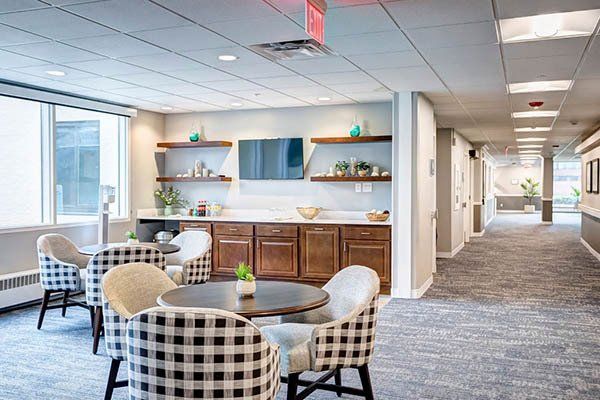 Lounge area with round tables, patterned chairs, TV, and shelves with décor; long hallway to the right.