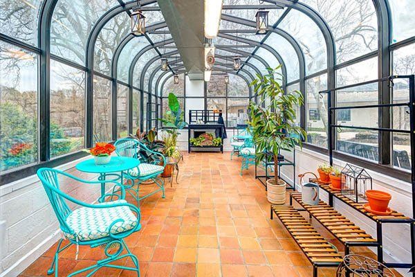 Sunroom with arched glass ceiling, terracotta tile floor, turquoise chairs, and potted plants.