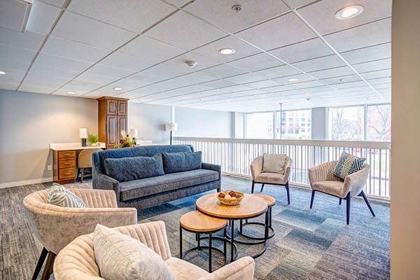 Lounge area with blue couch, armchairs, coffee tables, desk, and cabinets. Light colors and open space.