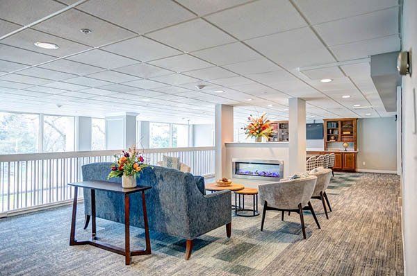 Lounge area with blue couch, armchairs, fireplace, and built-in shelves with floral decorations and large windows.