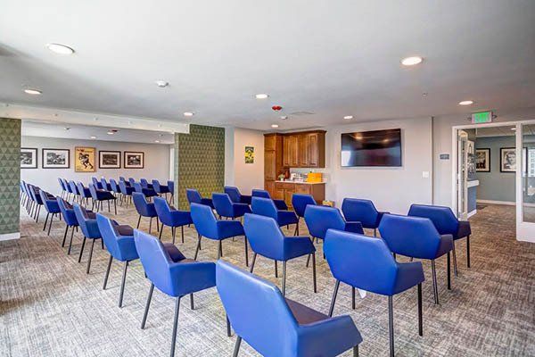 Auditorium with blue chairs arranged for a presentation. A TV screen and art are visible.
