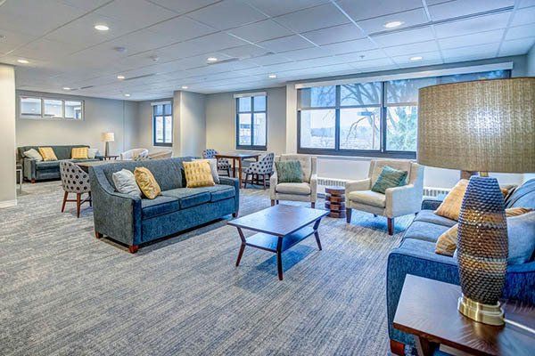 Spacious, well-lit lounge area with blue sofas, armchairs, and coffee tables on a patterned carpet.