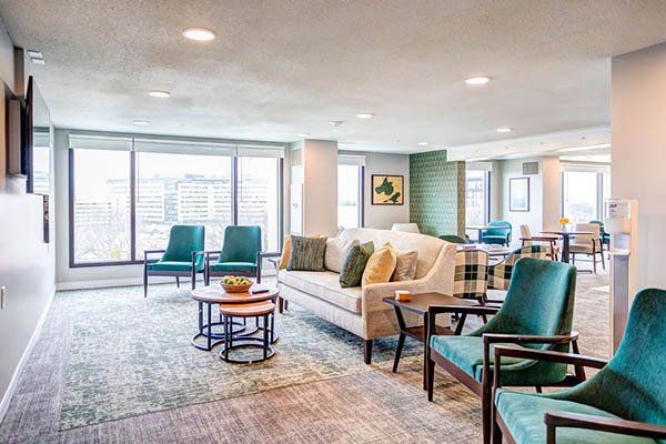 Spacious, well-lit lounge area with couches, chairs, and windows overlooking a city. Teal and neutral colors.