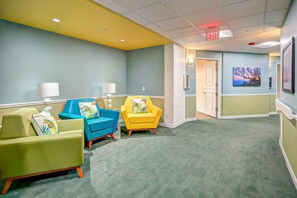 A waiting area with colorful chairs and a hallway. Blue and yellow walls, green carpet.