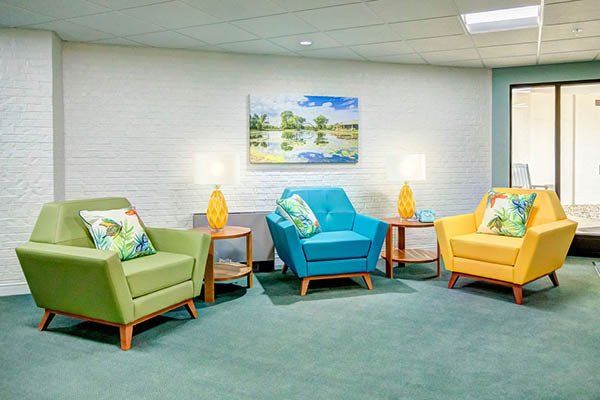 Three colorful armchairs in a waiting room with side tables, lamps, and a painting.