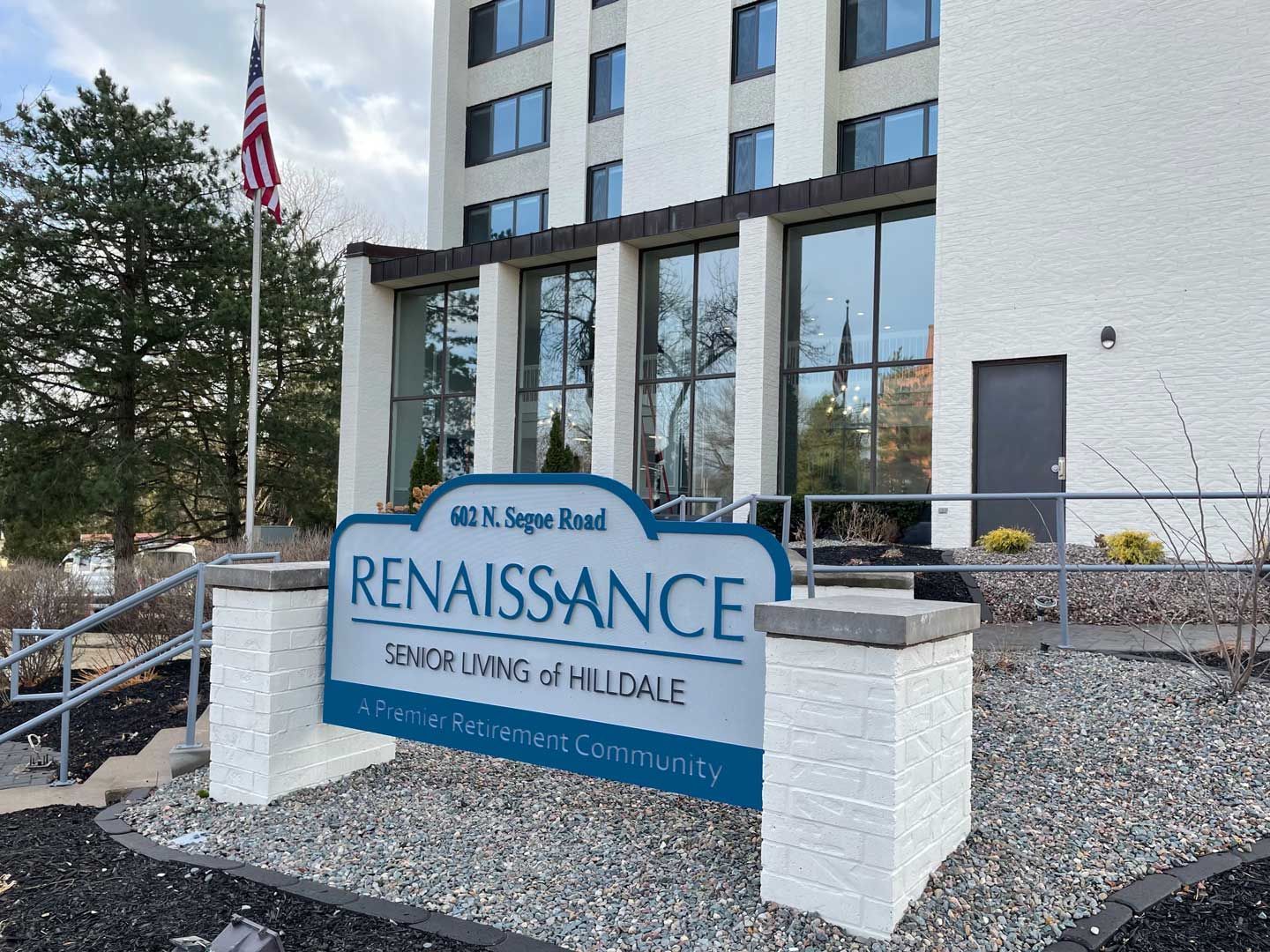 Sign for Renaissance Senior Living, with a building in the background and an American flag.