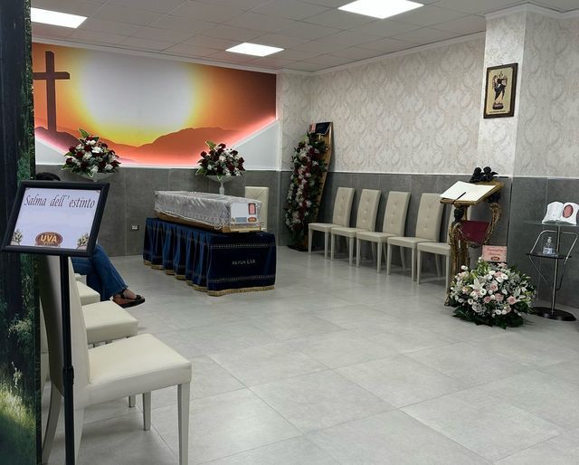 Una stanza con una bara e delle sedie e una croce sul muro casa funeraria uva