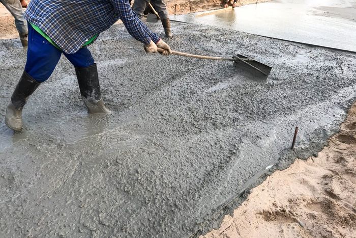 A man is spreading concrete on the ground with a shovel.
