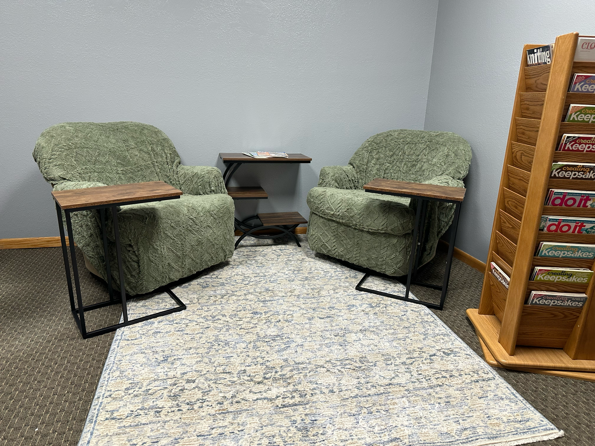 Two green armchairs with side tables on a rug, small side table between them, and a magazine rack.