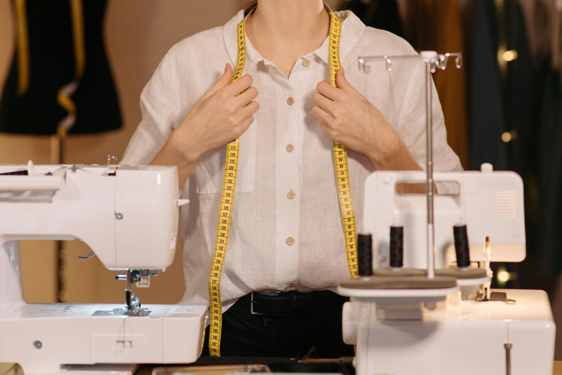 Seamstress with a tape measure around her neck, standing in front of sewing machines.