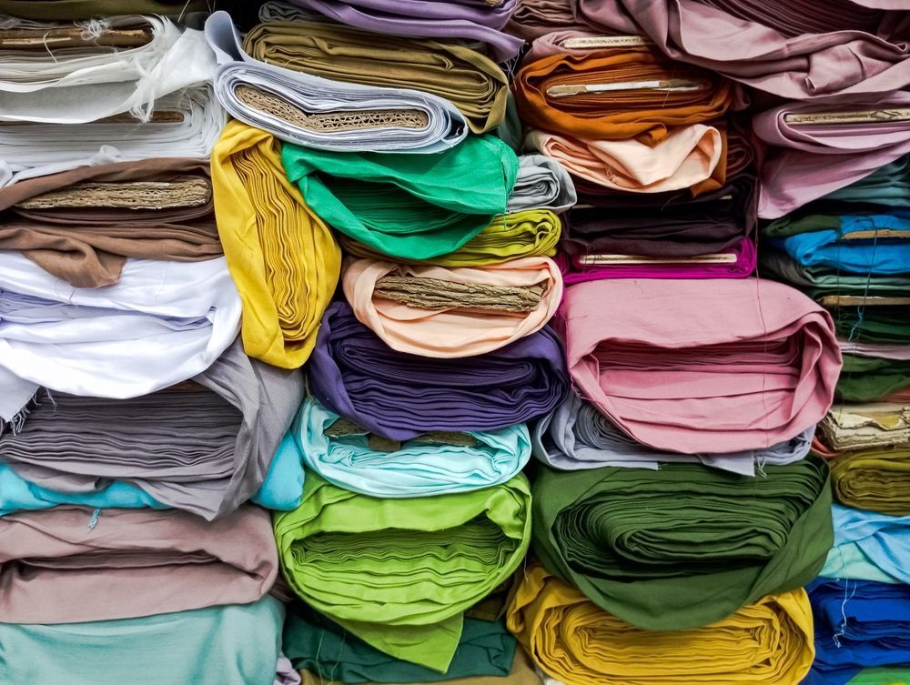 Fabric bolts stacked in various colors: green, blue, yellow, pink, purple, and brown.