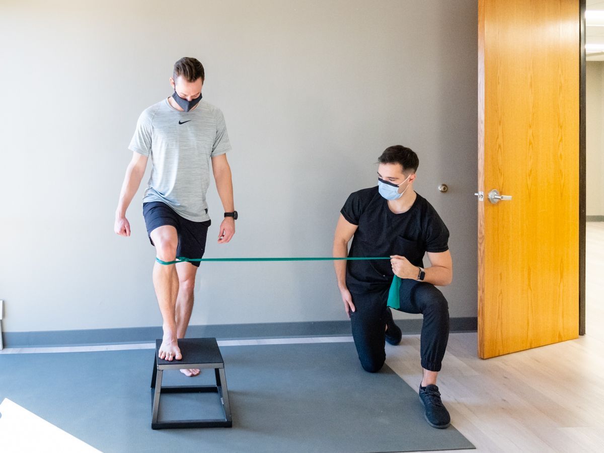 a man is kneeling down while another man stands on a box with a resistance band .