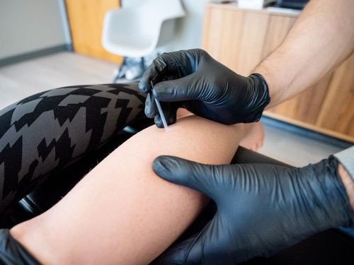 a man in a blue shirt is applying kinesio tape to a man 's knee