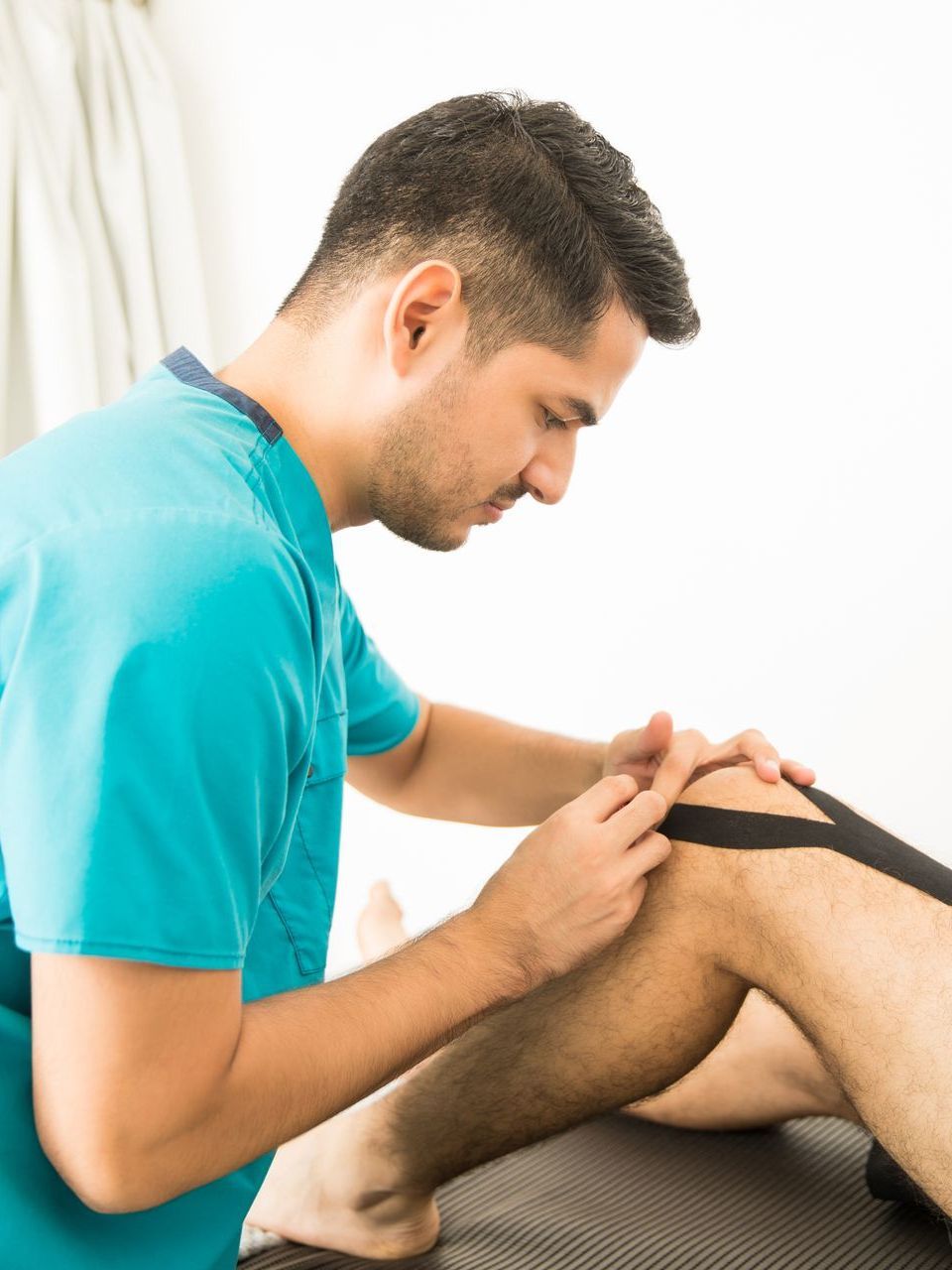 a man in a blue shirt is applying kinesio tape to a man 's knee