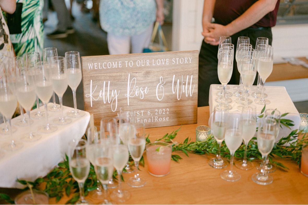 Wedding reception champagne display with sign, glasses, and greenery.