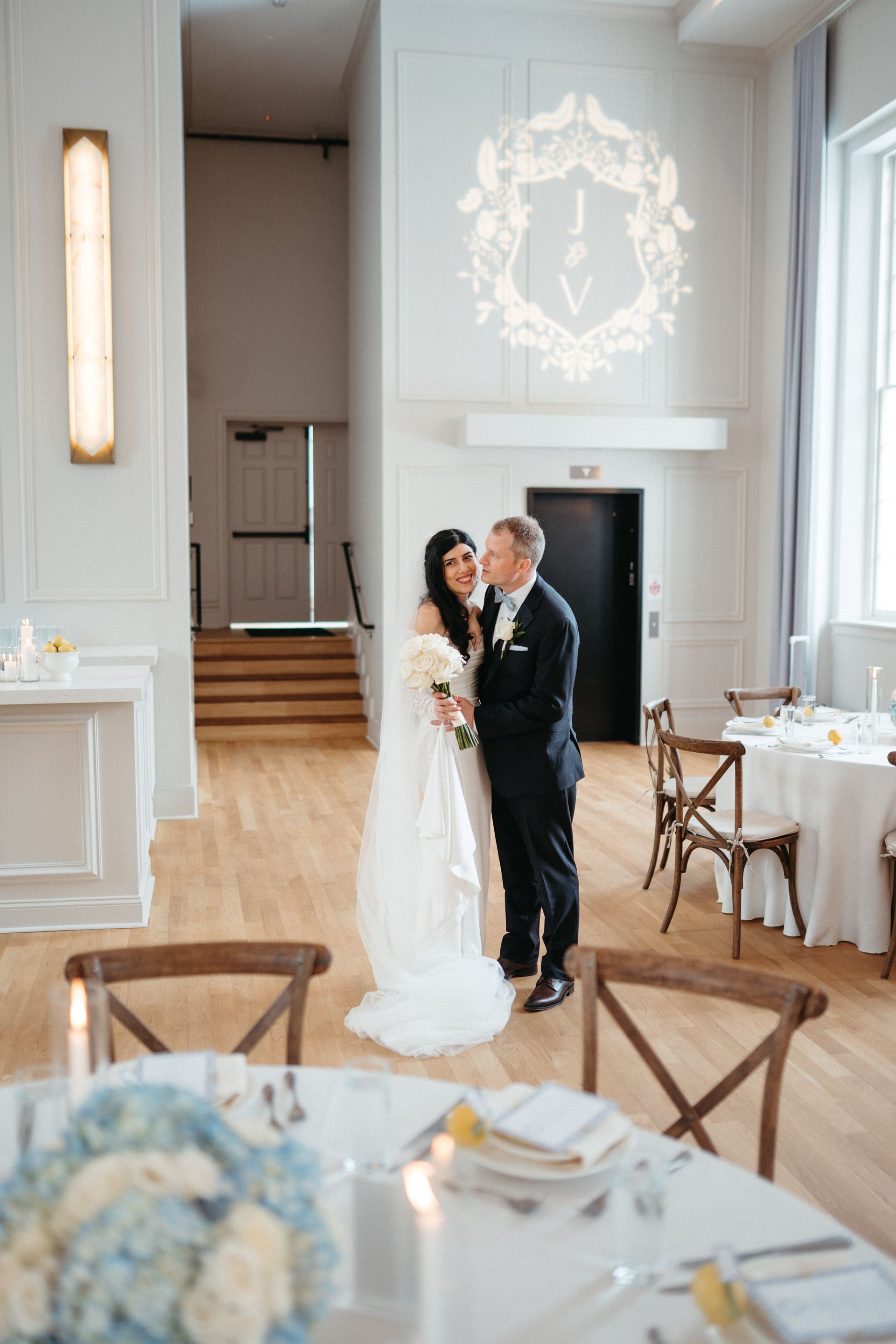 A bride and groom share a kiss in a bright wedding reception hall.