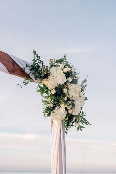 A wooden arch decorated with white flowers and greenery on the beach.